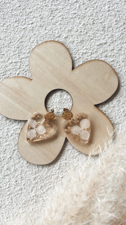Boucles d'oreilles en forme de cœur en résine avec des fleurs séchées incrustées et attaches en acier inoxydable.