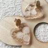 Boucles d'oreilles en forme de cœur en résine avec des fleurs séchées incrustées et attaches en acier inoxydable.