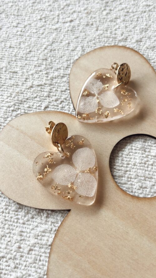 Boucles d'oreilles en forme de cœur en résine avec des fleurs séchées incrustées et attaches en acier inoxydable.