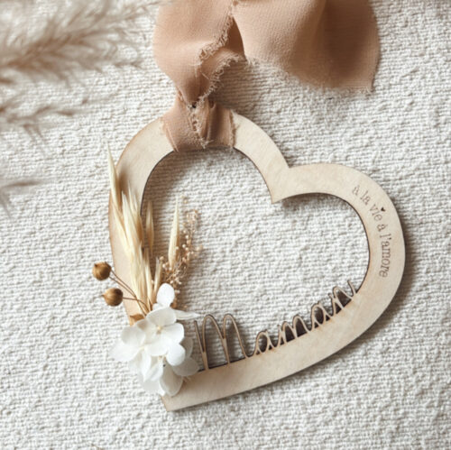 Suspension en bois en forme de cœur avec l'inscription 'À la vie à l'amour' et des fleurs séchées, ornée d'un ruban beige.