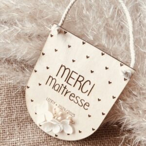 Suspension en bois personnalisable 'Merci Maîtresse' avec des fleurs séchées et le prénom de votre choix gravé, ornée de petits cœurs.