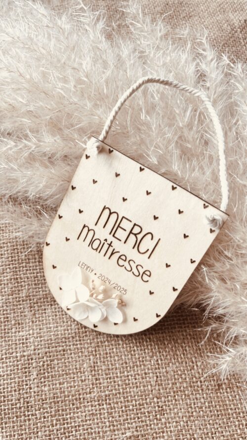 Suspension en bois personnalisable 'Merci Maîtresse' avec des fleurs séchées et le prénom de votre choix gravé, ornée de petits cœurs.