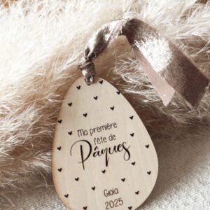 Médaillon décoratif en bois gravé 'Ma première fête de Pâques' avec personnalisation orné d'un ruban doré.