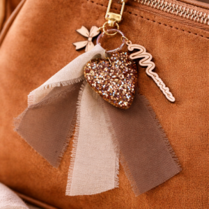 Porte-clé Mamie avec cœur pailleté doré, breloques en bois et ruban beige accroché à un sac, création artisanale fait main.